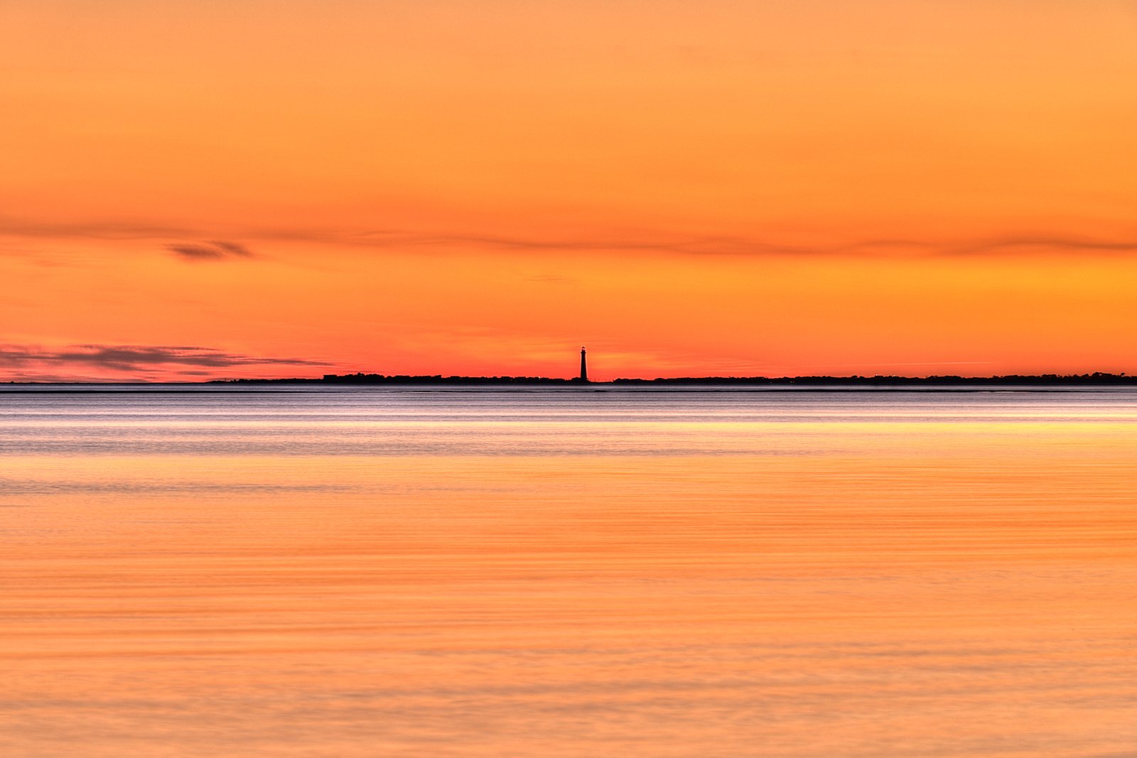 Sunset over calm water with lighthouse silhouette near Sullivan's Island